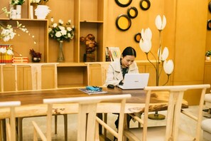 Una persona treballant a una taula de fusta amb un ordinador portàtil, envoltada de llibres i objectes decoratius en una habitació amb llum càlida.