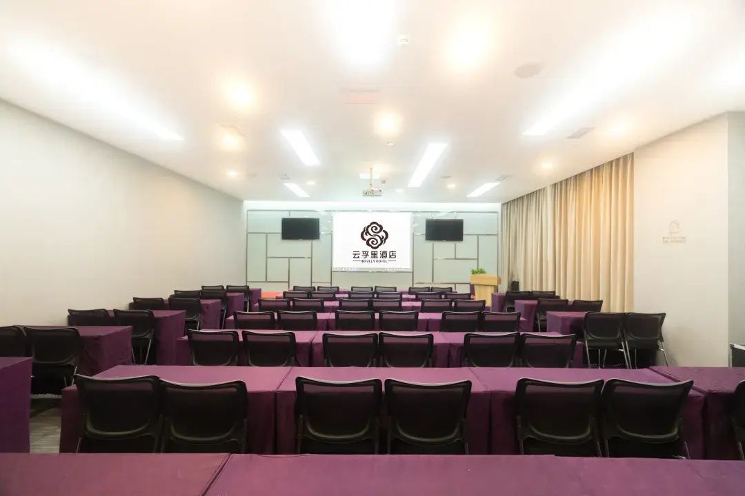 Un salón de conferencias con mesas y sillas dispuestas en filas, un escenario con un banner y un atril.