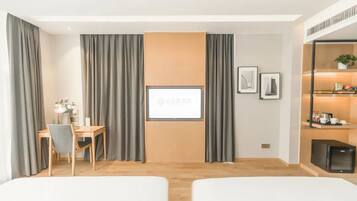Habitación de hotel con dos camas, un escritorio, una silla, un refrigerador pequeño y una televisión en la pared.