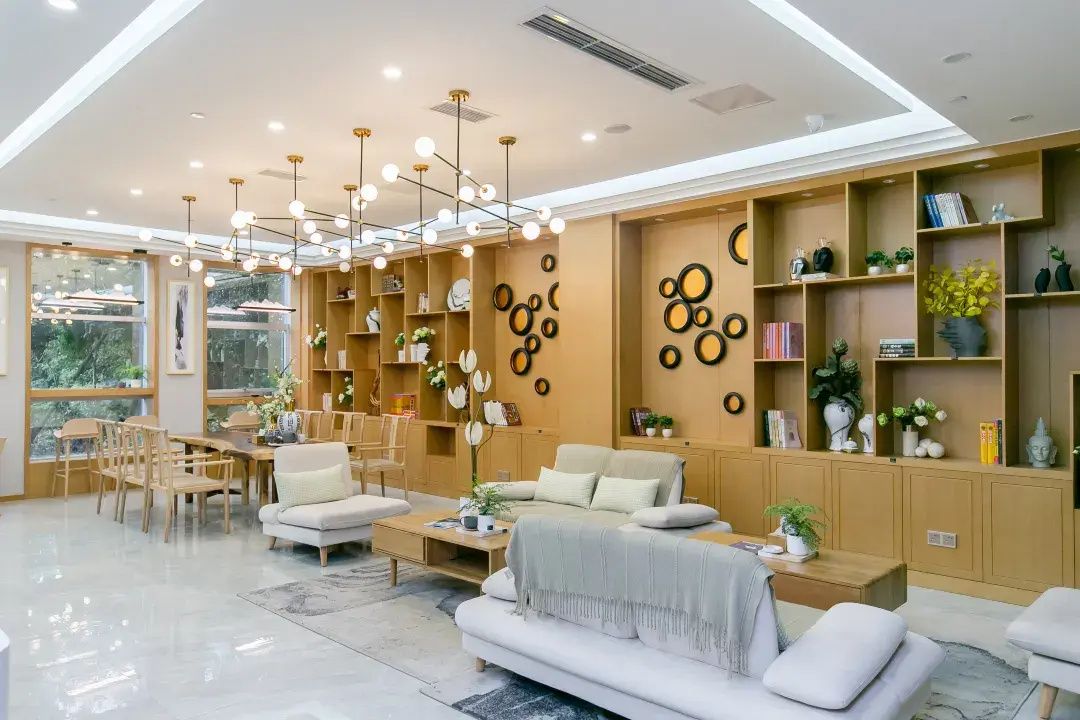 Una sala moderna con sofá, mesa de centro y comedor. Hay estanterías con objetos decorativos y un candelabro en el techo.