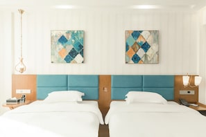 A hotel room with two beds, a headboard, a nightstand, a lamp, and two abstract paintings on the wall. - Yunfuli Hotel Long'an Station (Chengdu)
