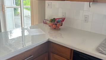 A kitchen with wooden cabinets, a white countertop, a dish rack with fruits, and a dishwasher.