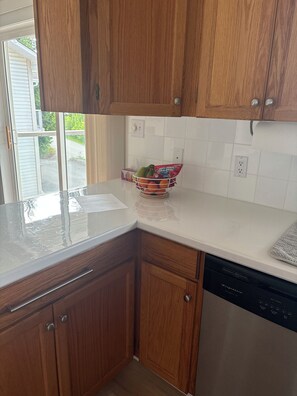 Una cocina con armarios de madera, encimera blanca, un escurreplatos con frutas y un lavavajillas.