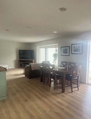 Uma sala de jantar com uma mesa e cadeiras de madeira, uma televisão e uma janela com persianas.