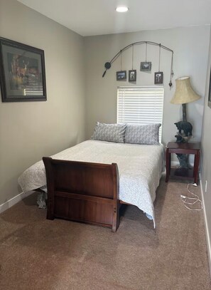 Un dormitorio con cama, mesita de noche, lámpara y estante con fotografías.