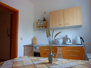A small kitchen with a tiled table, two chairs, a coffee maker, a kettle, and a cabinet above the counter. - mit zwei Doppel- und einem Einzelzimmer, Essküche, Vollbad und Balkon by Interhome (Küstriner Vorland)