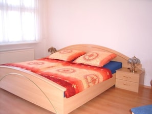 A bedroom with a wooden bed, a nightstand, and a lamp. - mit zwei Doppel- und einem Einzelzimmer, Essküche, Vollbad und Balkon by Interhome (Küstriner Vorland)