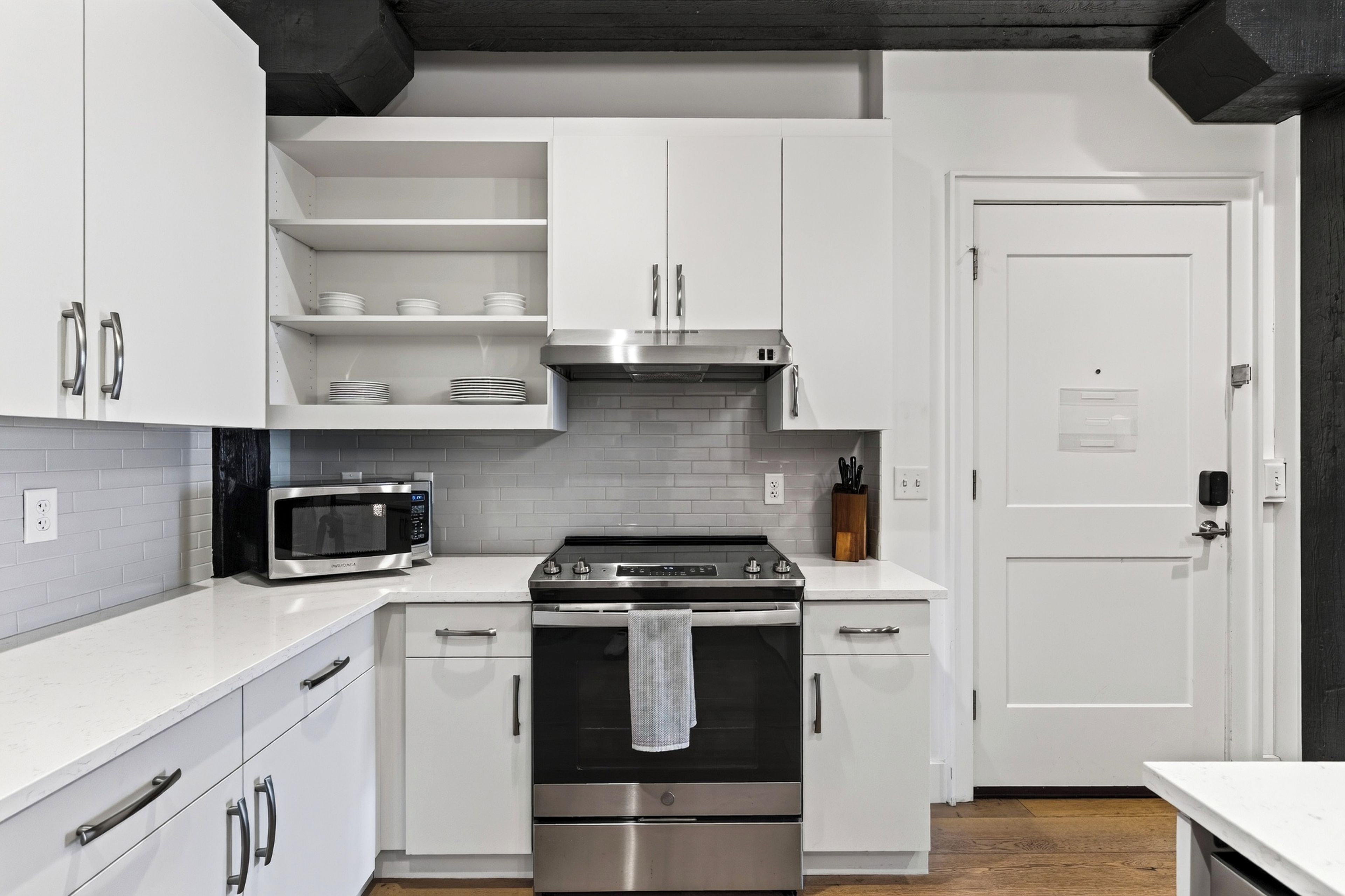 A modern kitchen with white cabinetry, a stainless steel oven, a microwave, and a black range hood.