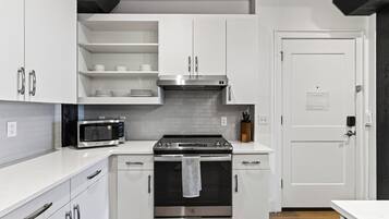 A modern kitchen with white cabinetry, a stainless steel oven, a microwave, and a black range hood.