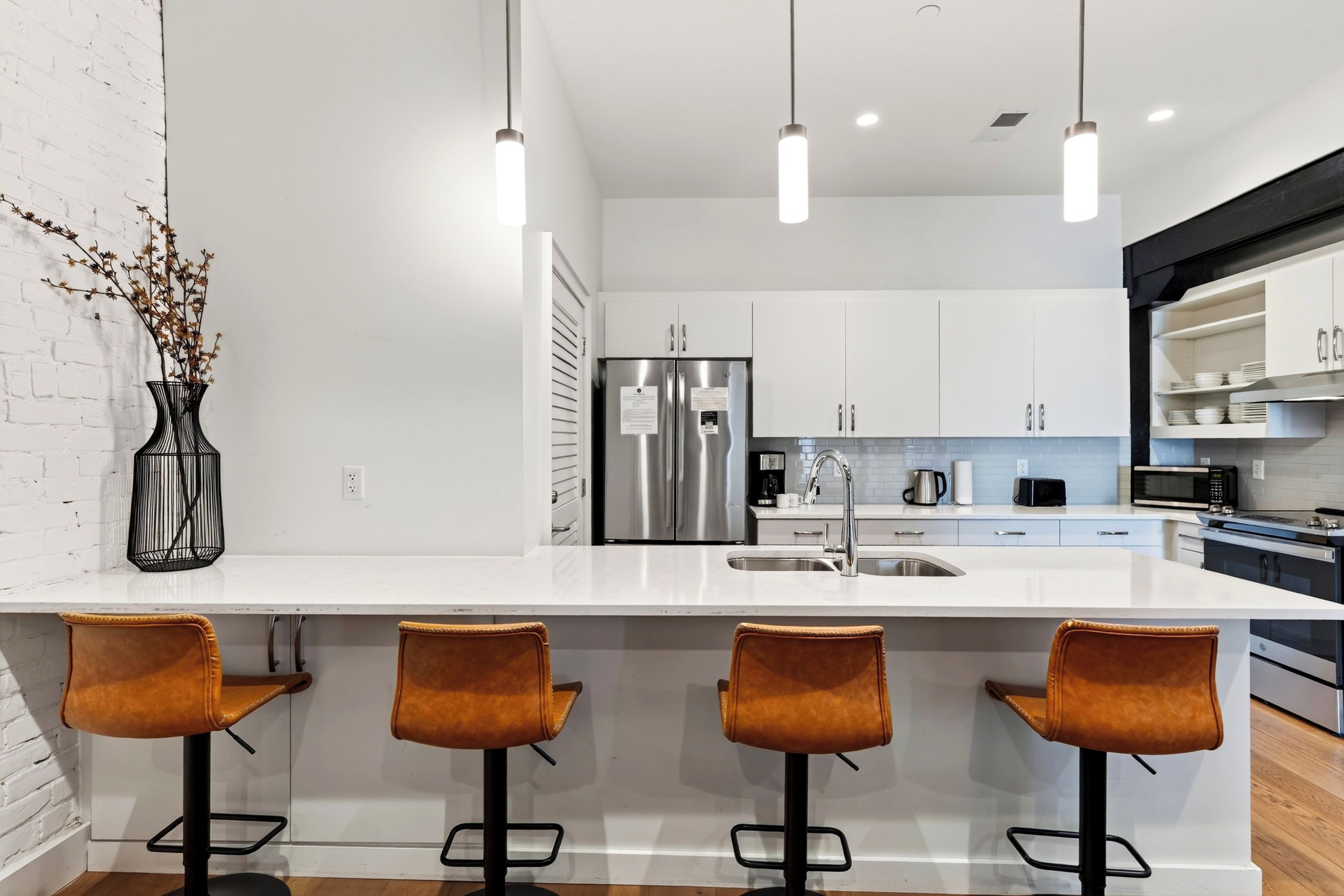 Una cocina moderna con encimera blanca, electrodomésticos de acero inoxidable y tres taburetes de bar.