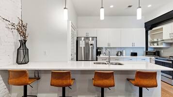 Una cocina moderna con encimera blanca, electrodomésticos de acero inoxidable y tres taburetes de bar.