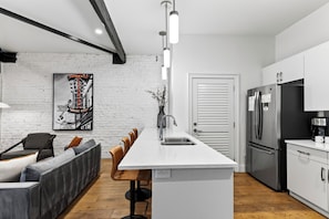 Una cocina moderna con una isla central, electrodomésticos de acero inoxidable y una pared de ladrillo blanco.