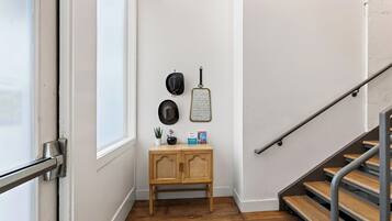 Un pasillo con piso de madera, un mueble de madera pequeño y una escalera con barandillas de metal.