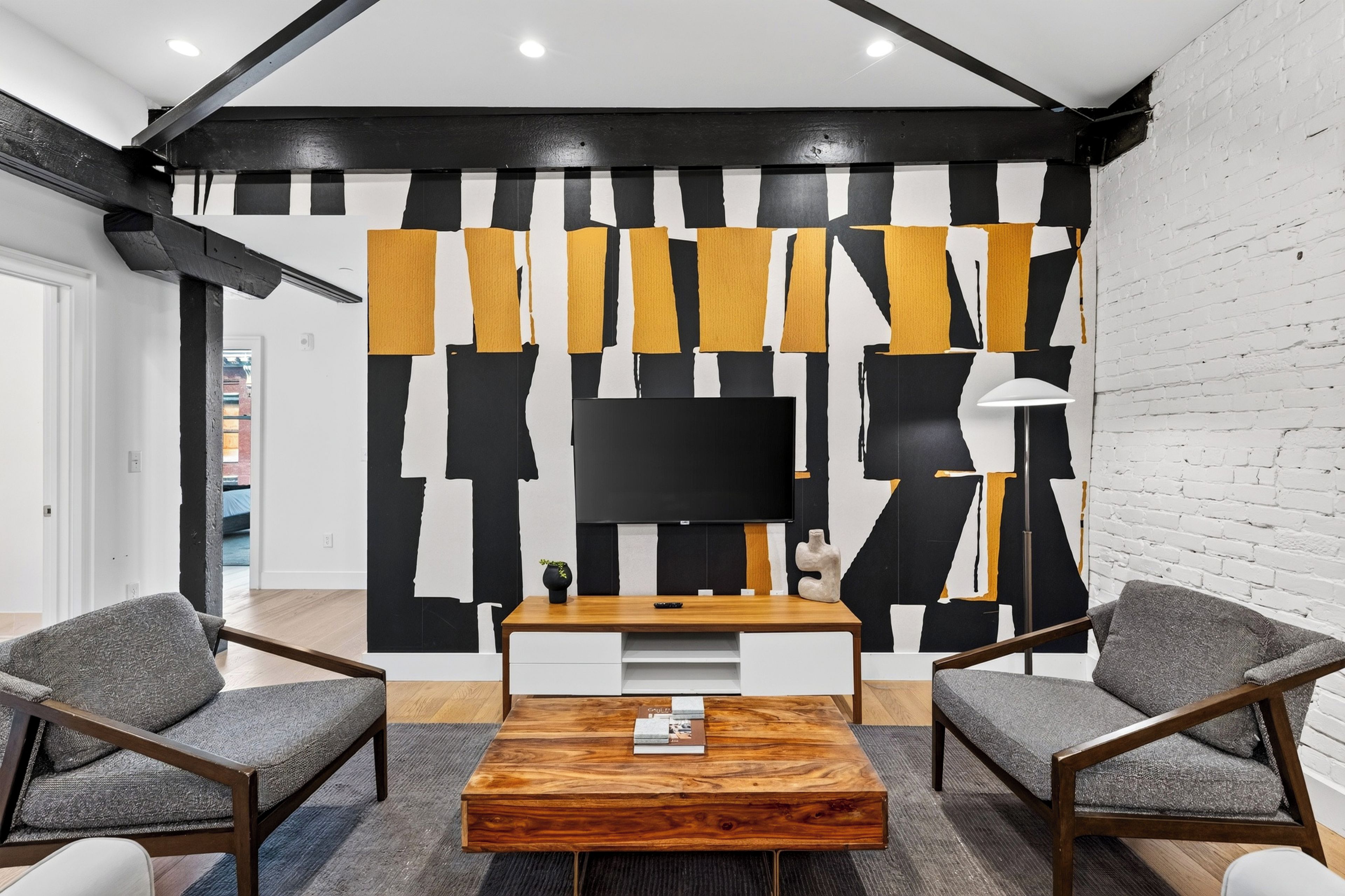 A modern living room with a black and white abstract wall art, a flat-screen TV, and a wooden coffee table.