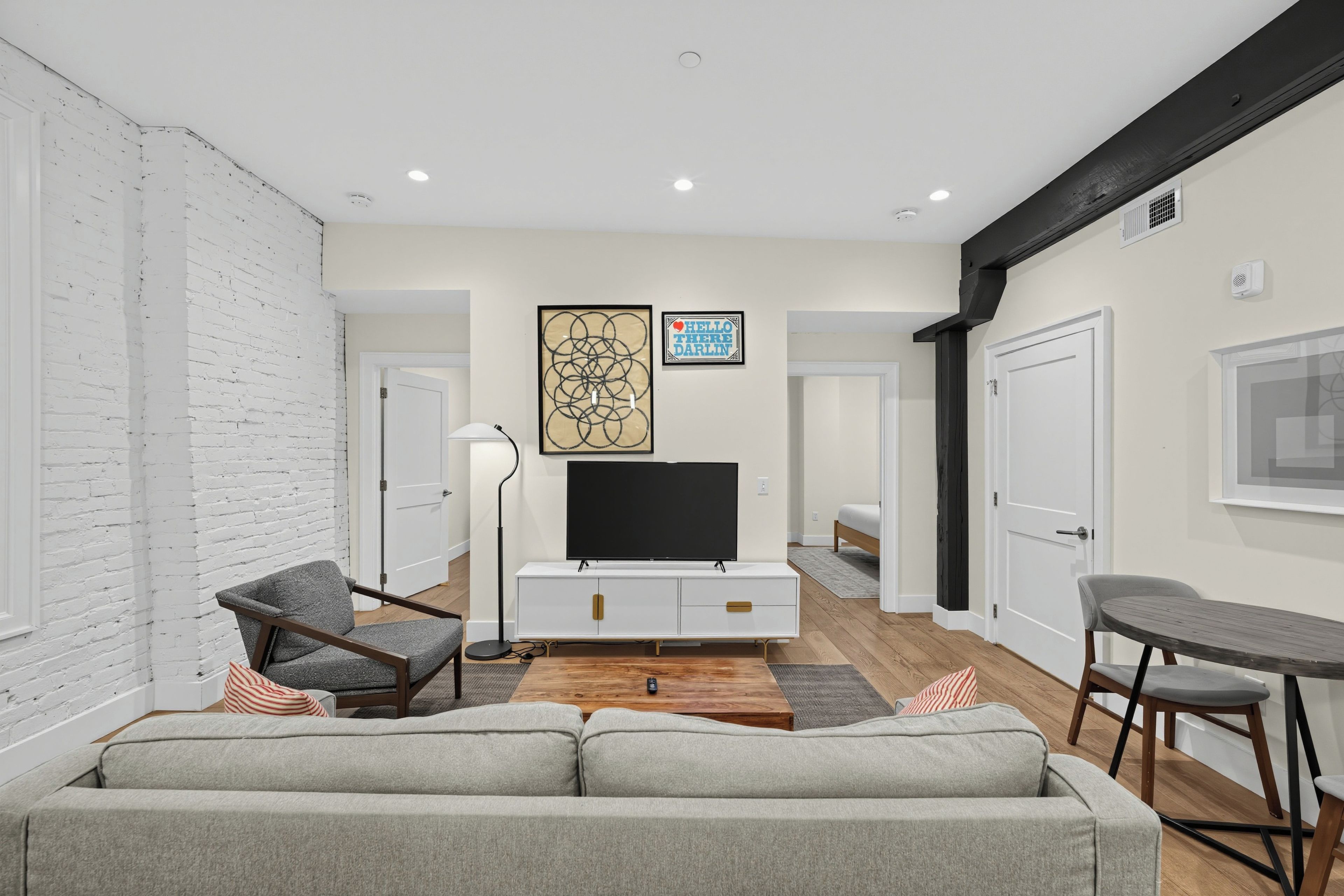 A modern living room with a sofa, a TV on a white cabinet, a floor lamp, and a painting on the wall.