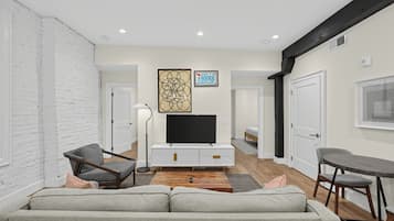 A modern living room with a sofa, a TV on a white cabinet, a floor lamp, and a painting on the wall.