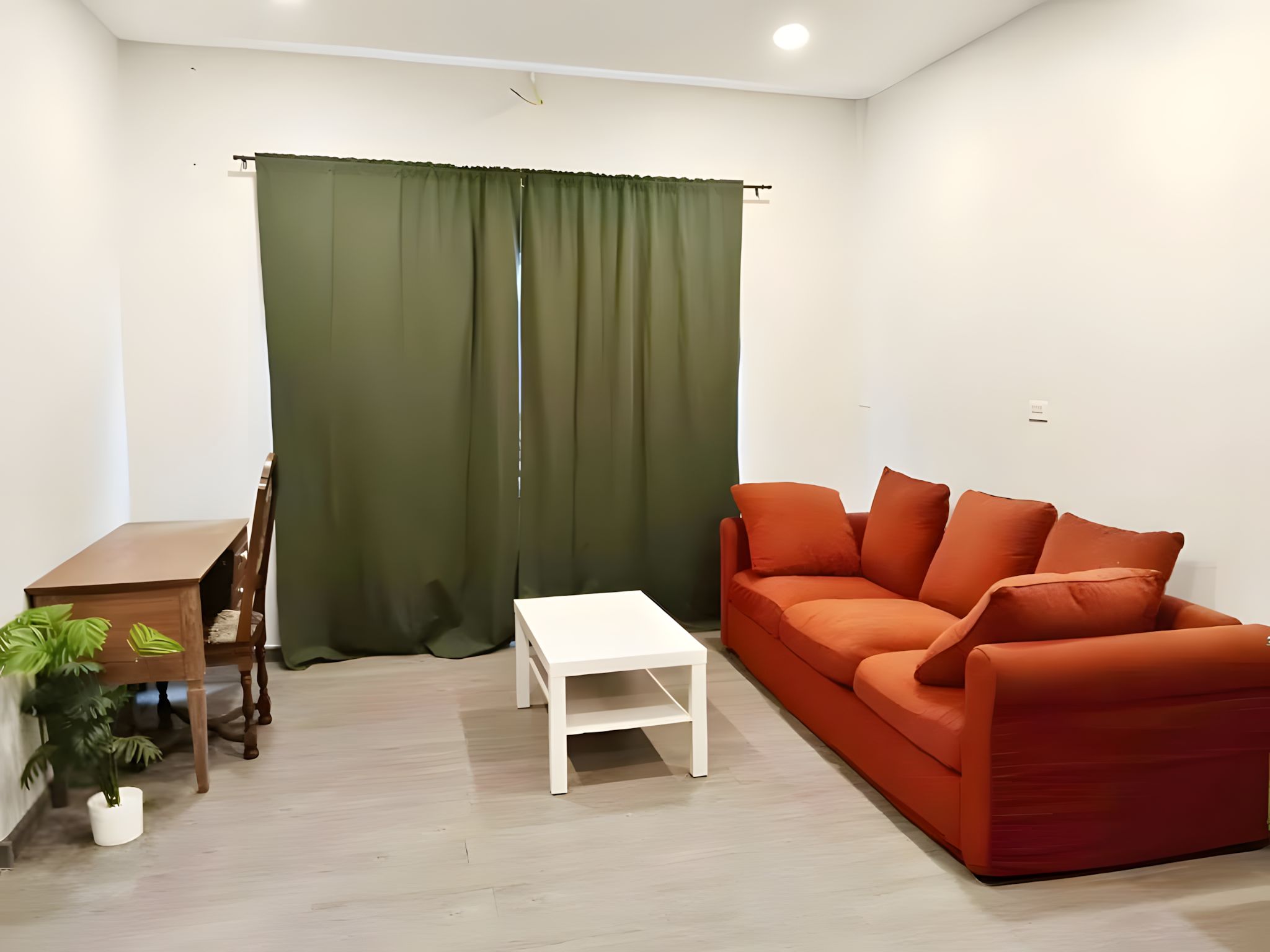 A living room with a wooden table, a white coffee table, and an orange sofa.