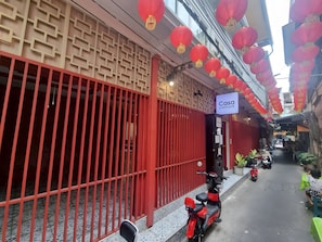 Une ruelle étroite avec une porte rouge, une enseigne indiquant « Casa Yaowarat », et un scooter garé sur le bord.