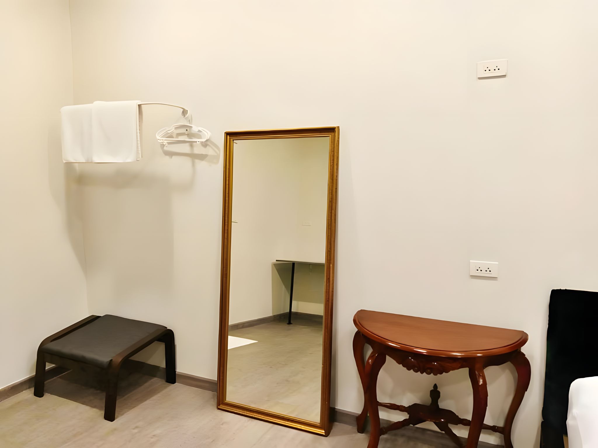 A room with a large mirror, a small stool, and a wooden table.