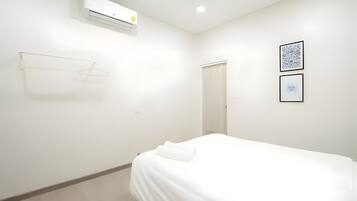 A minimalist hotel room with a bed, a wall-mounted air conditioner, a door, and two framed artworks.