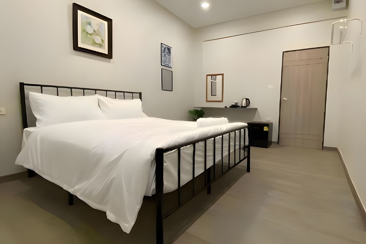 A bedroom with a bed, a bedside table, a nightstand, a door, and a wall-mounted light fixture.