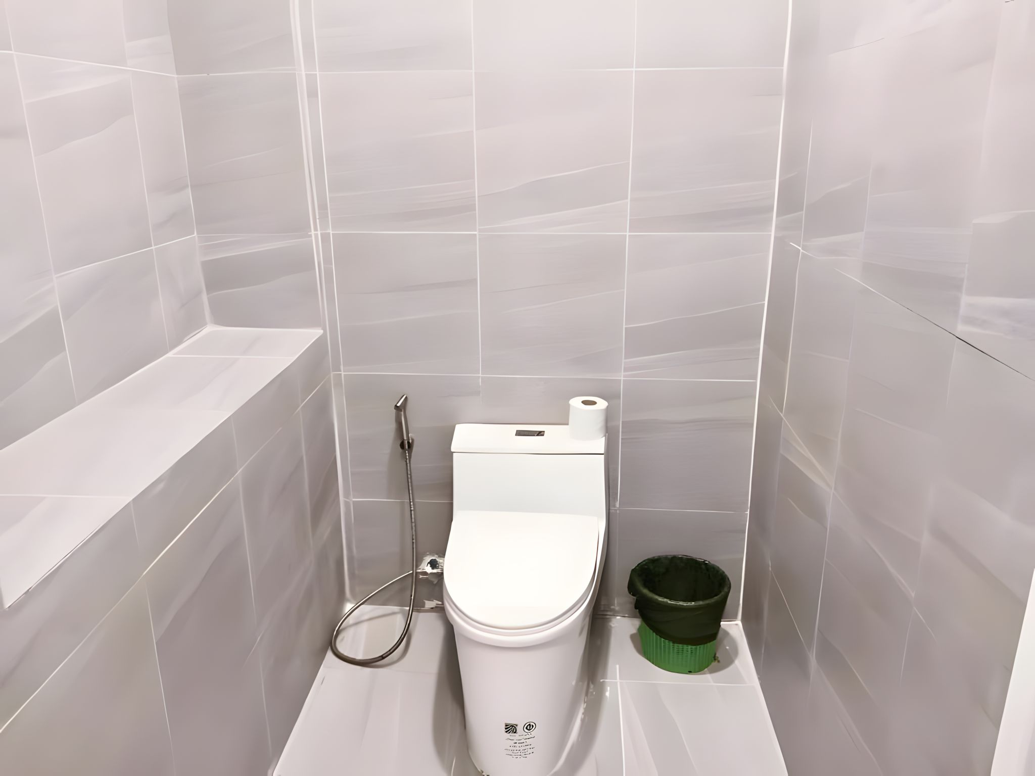 A small, modern bathroom with a toilet, a green trash bin, and a shower head.
