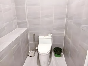 Une petite salle de bain moderne, équipée de toilettes, d’une poubelle verte et d’un pommeau de douche.