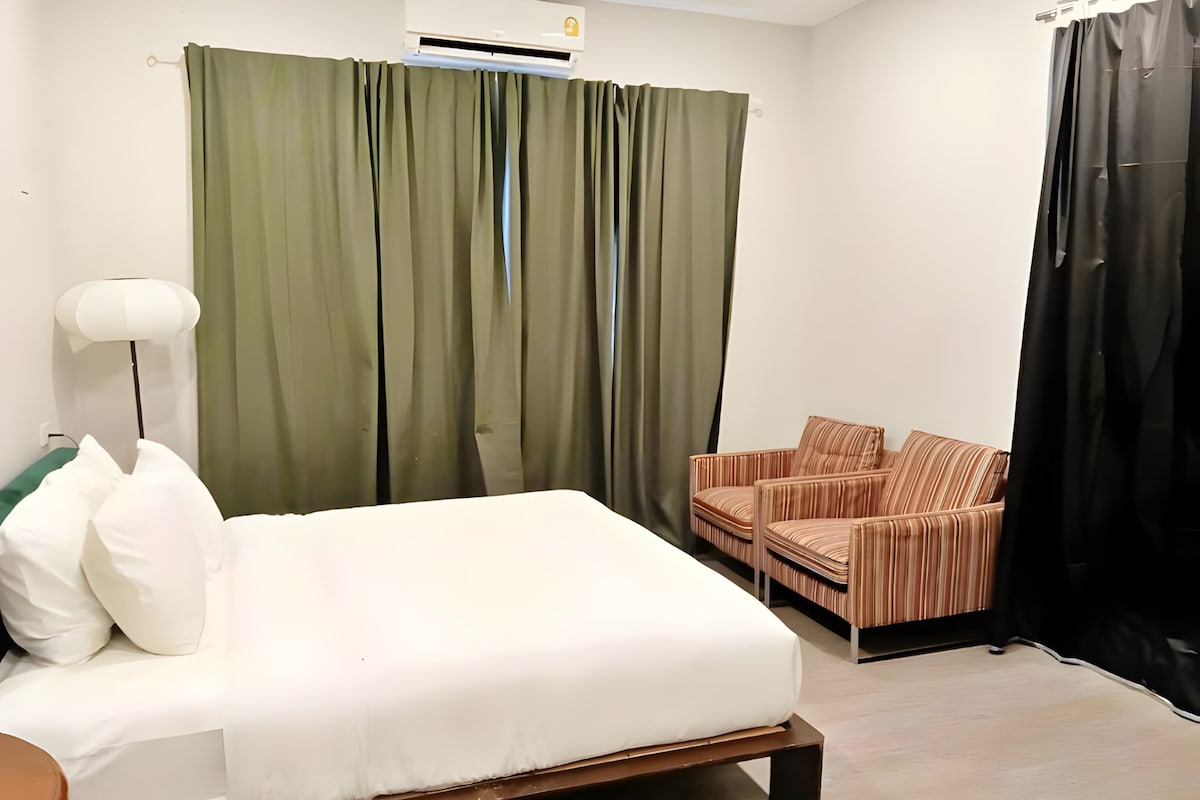 A hotel room with a bed, a chair, a lamp, and a curtain.