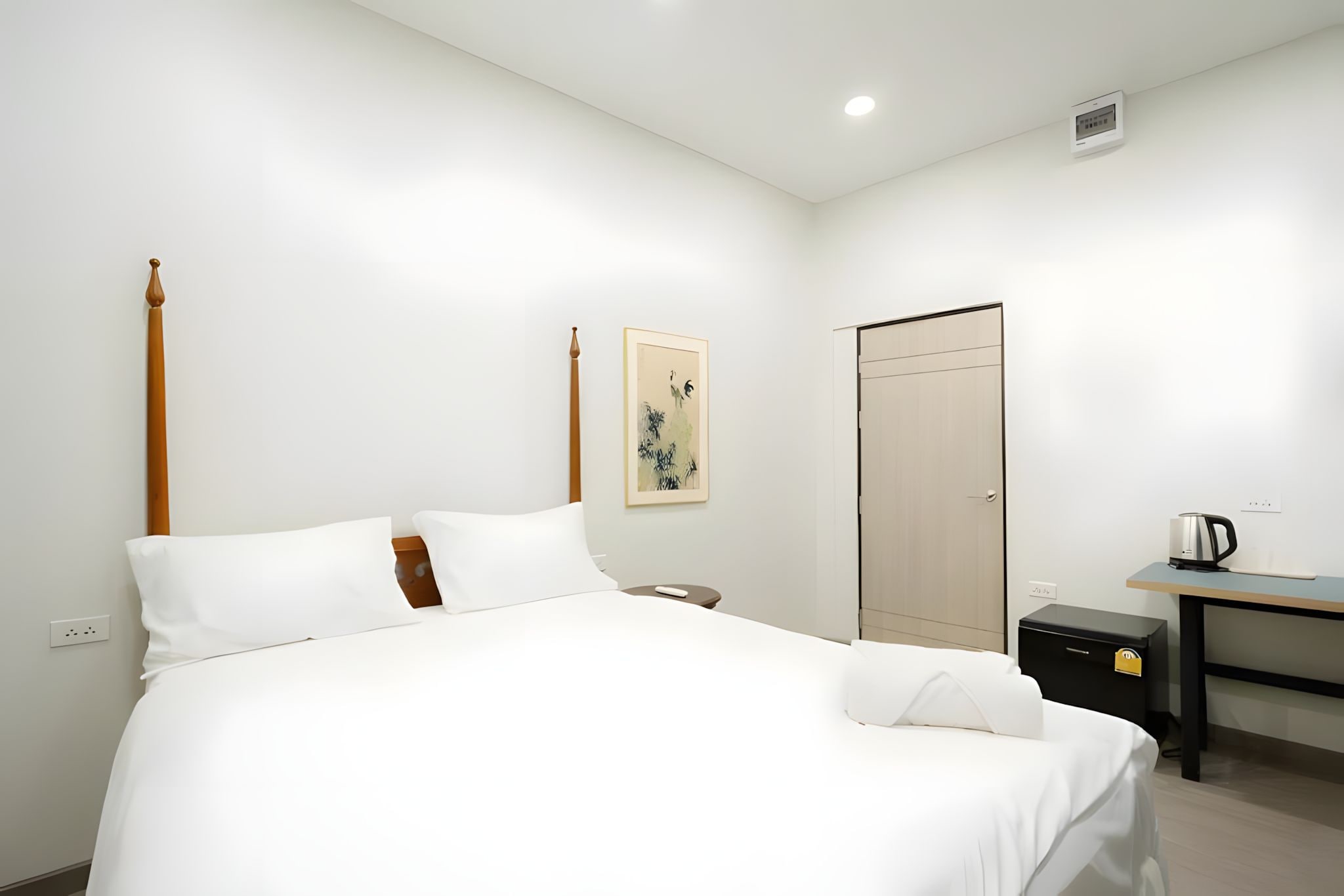 A hotel room with a bed, a desk, a chair, a wardrobe, and a painting on the wall.