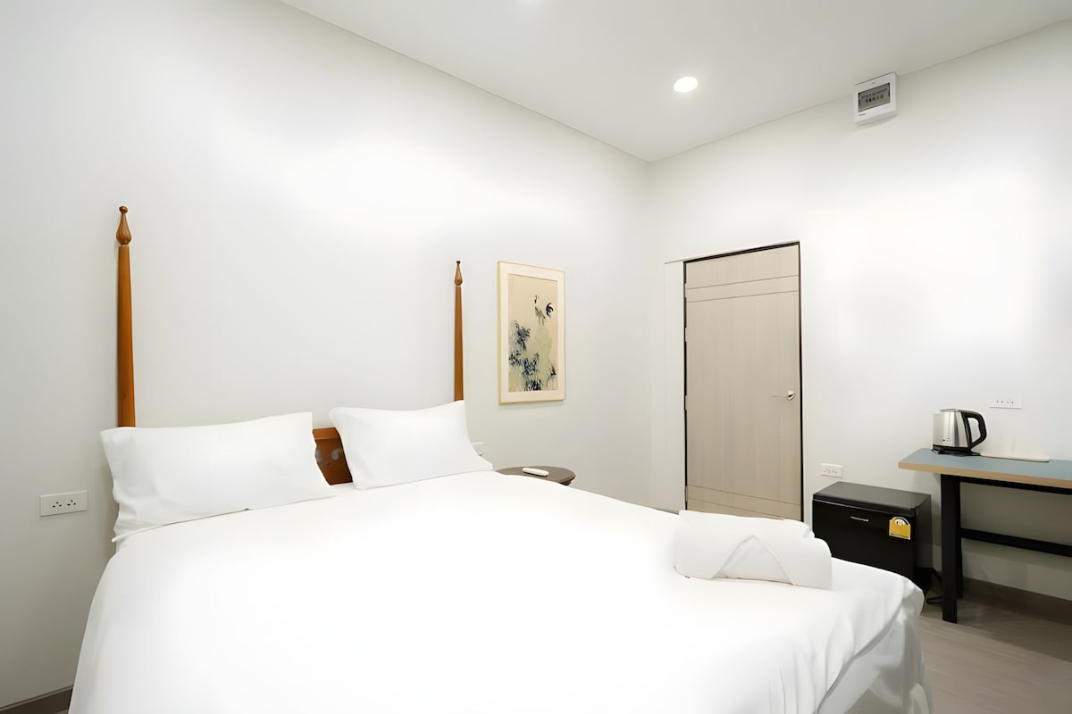 A hotel room with a bed, a desk, a chair, a wardrobe, and a painting on the wall.