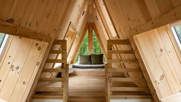 A wooden attic bedroom with a loft bed, a window, and a view of greenery outside.