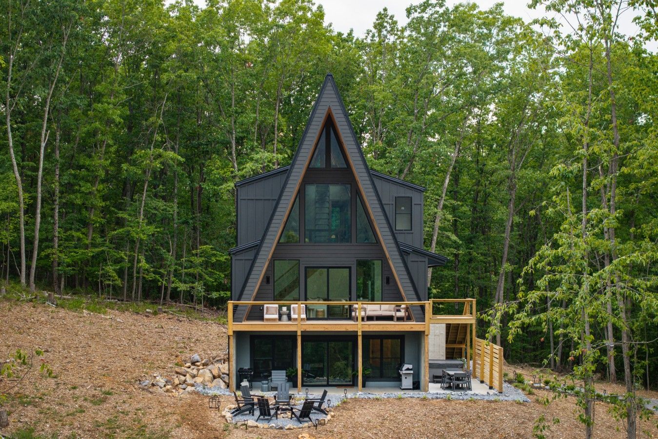 Una cabaña moderna tipo A con terraza, rodeada de un bosque denso.