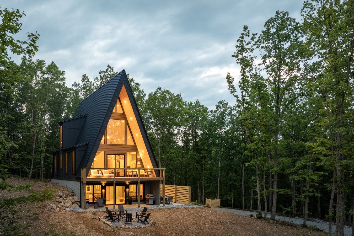 A modern house with a triangular roof, large windows, and a deck with outdoor seating.