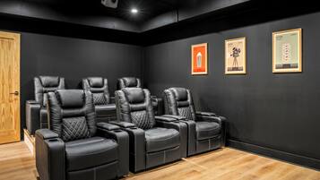 Un cine en casa con sillones reclinables de cuero negro, una puerta de madera y carteles de películas enmarcados en la pared.