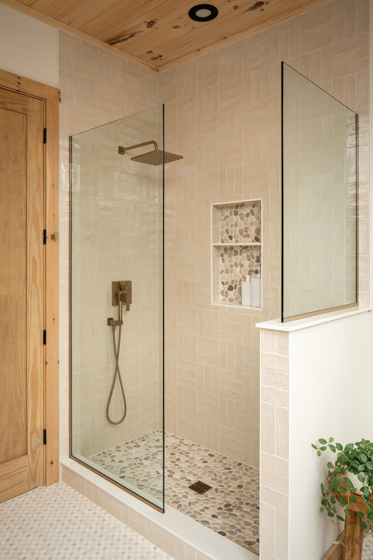 A glass-enclosed shower with a handheld showerhead and a wall-mounted control panel.