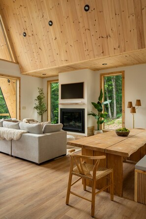 A spacious living room with a fireplace, a dining table, and a sofa. - Solhaus Shenandoah A-Frame | Park Views, Hot Tub, Theater & Game Room (Luray)
