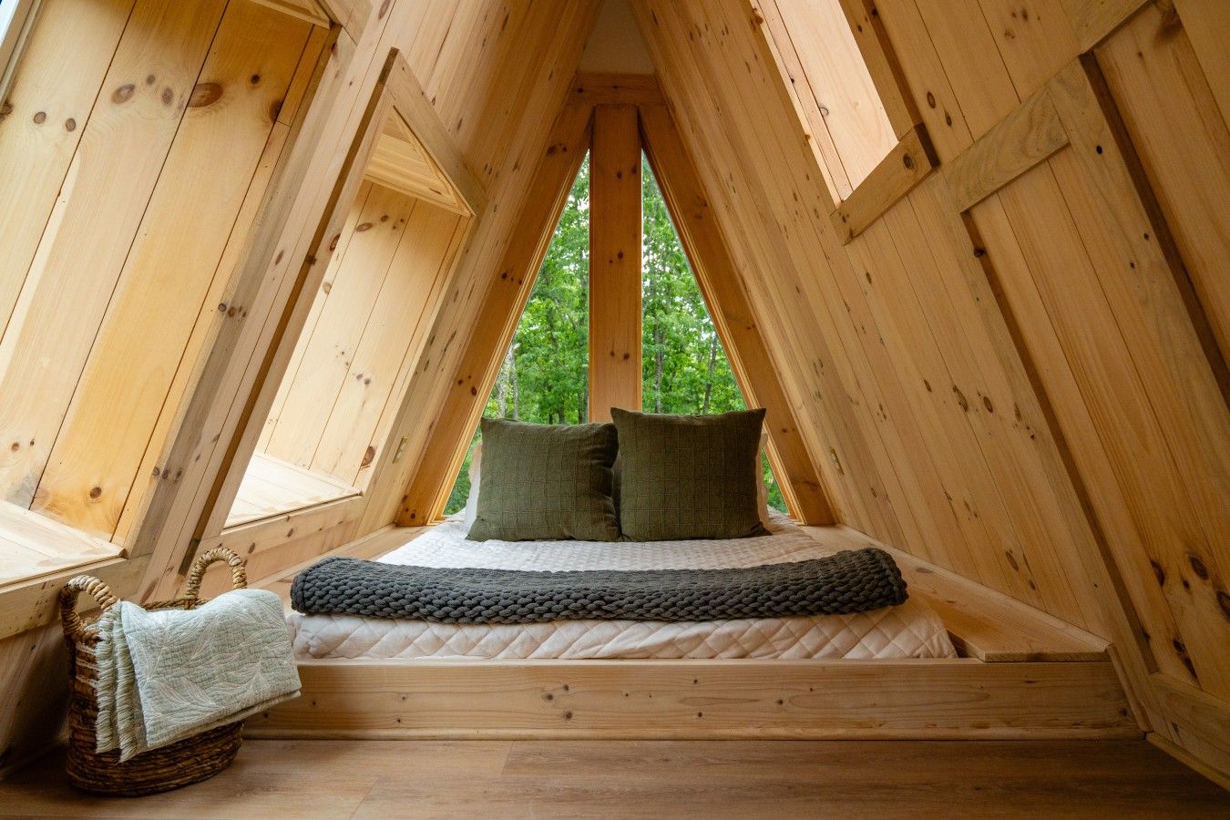 A triangular attic bedroom with a bed, pillows, and a basket.