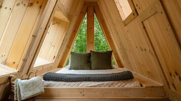 A triangular attic bedroom with a bed, pillows, and a basket.