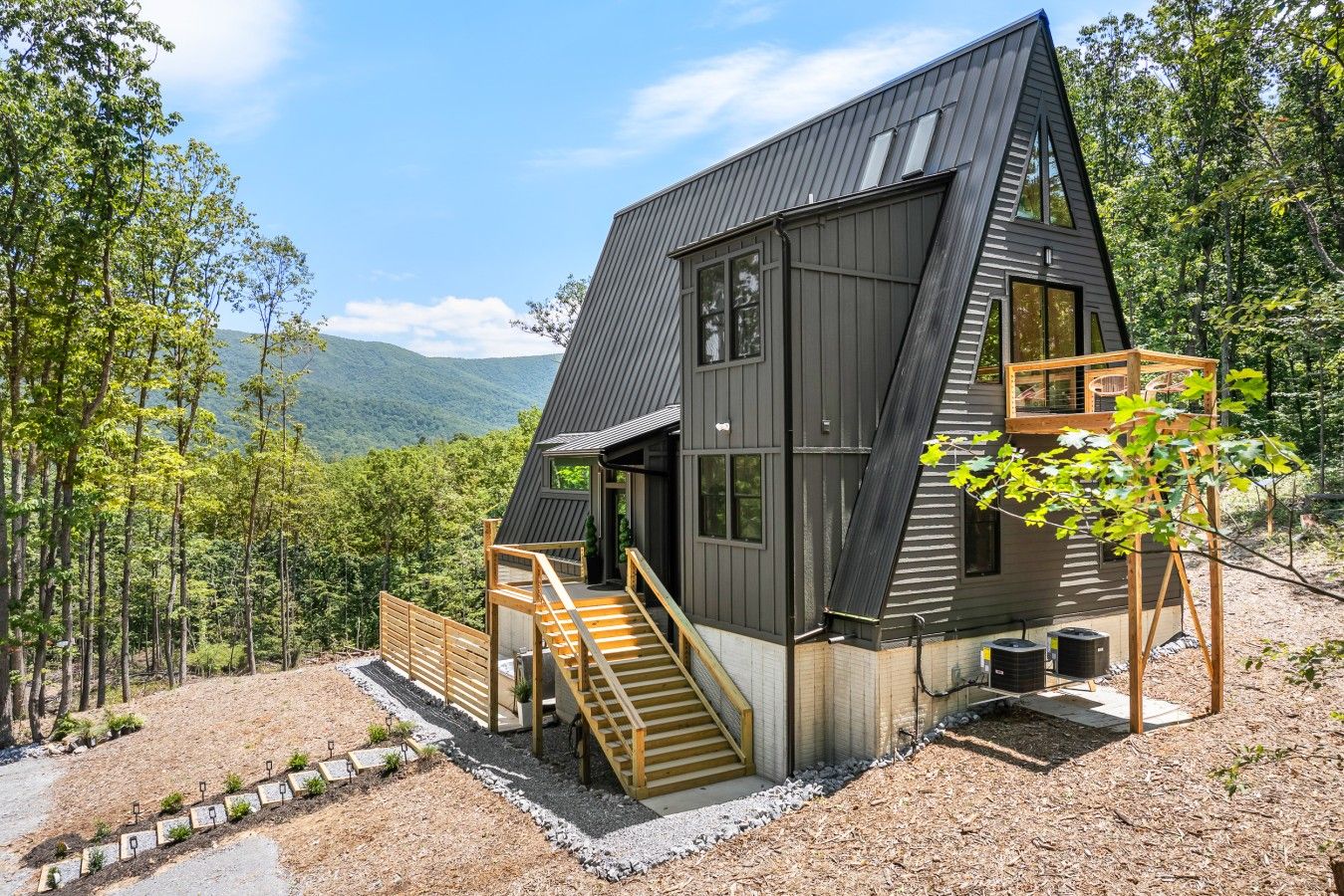 A modern, dark-colored cabin with a steeply pitched roof, a wooden staircase, and a small deck area.