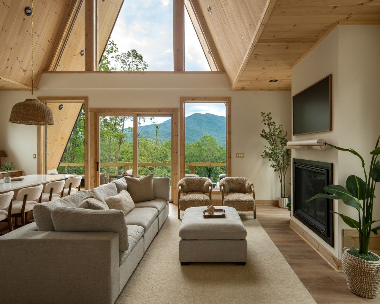 A spacious living room with a high ceiling, large windows, a fireplace, and a television.