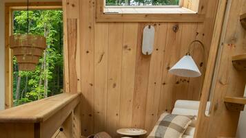 Interno di una baita di legno con un letto, una lampada a sospensione e una finestra vista foresta.