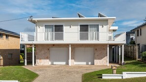 Un immeuble résidentiel de deux étages doté d’un balcon, de deux portes de garage et d’une façade en pierre.