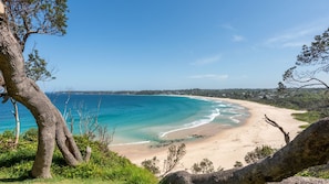 Un paysage côtier avec une plage de sable, des eaux d’un bleu limpide et une côte lointaine.