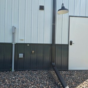 Fachada de un edificio con puerta metálica, teclado de seguridad, luminaria y conducto de ventilación.