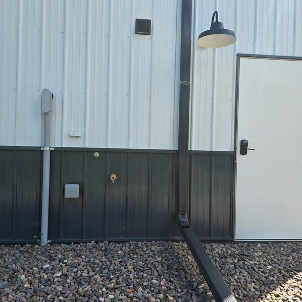 A building exterior with a metal door, a security keypad, a light fixture, and a ventilation pipe.