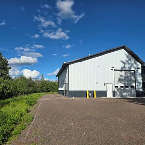 A large industrial building with a flat roof, a single garage door, and a gravel driveway. - Not Your Average Driveway (Duluth)