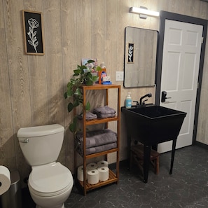 Un baño con inodoro, un estante con toallas, lavabo y espejo.