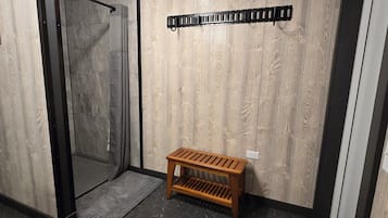 Habitación con pared de madera, un banco, zona de ducha y suelo de baldosas.
