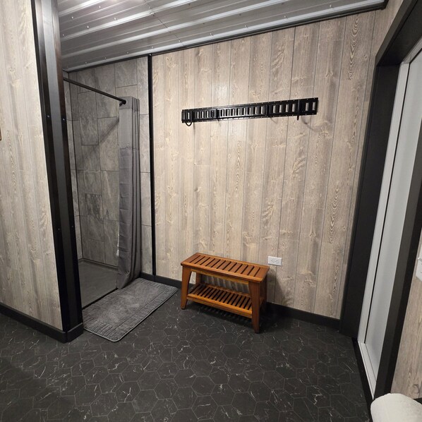 A room with a wooden wall, a bench, a shower area, and a tiled floor.