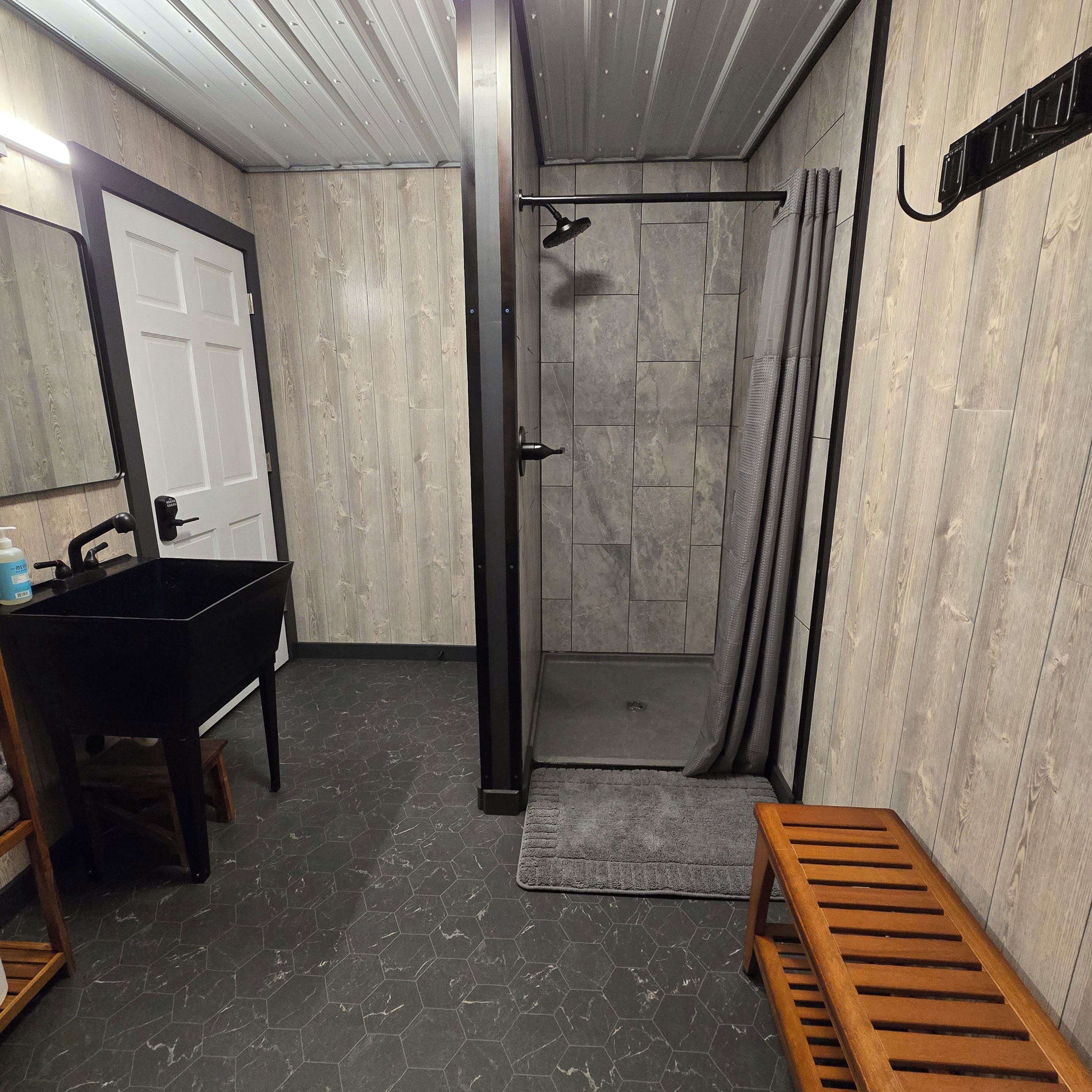 Un baño con ducha, lavamanos y un banco.